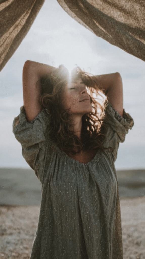 connect-nature-nervous-system-stretching3 Woman enjoying sunlight at the beach with eyes closed, basking in serenity and nature's beauty.