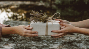 Hands exchanging a rustic gift wrapped with twine and dried flowers, set on a stone surface.