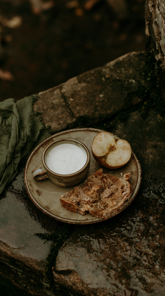 Rustic ceramic plate with cup of milk, sliced apple, and crusty bread on wet stone outdoors